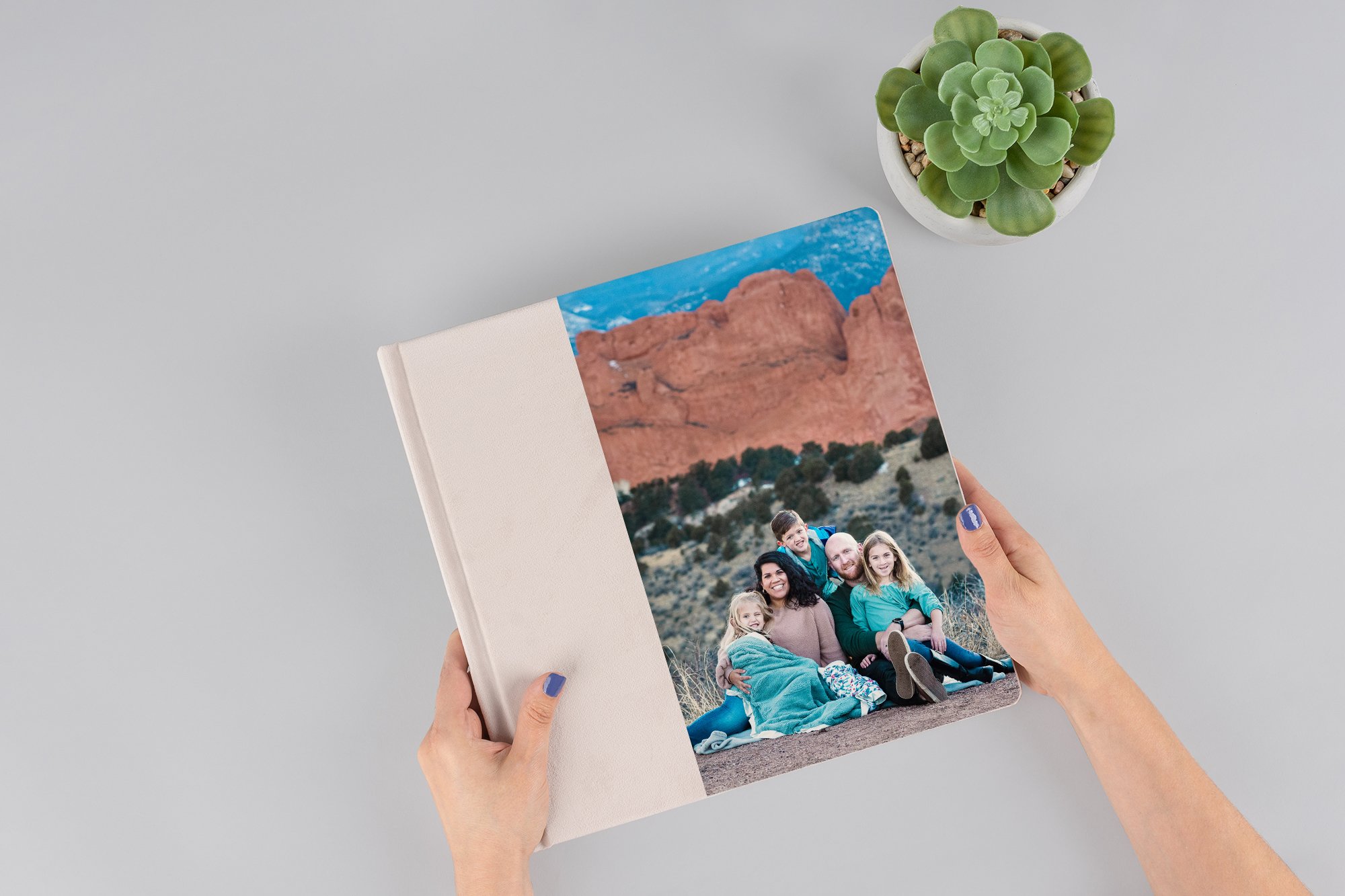 A couple holding hands and walking through a grassy field with mountains in the background, during a cloudy day.