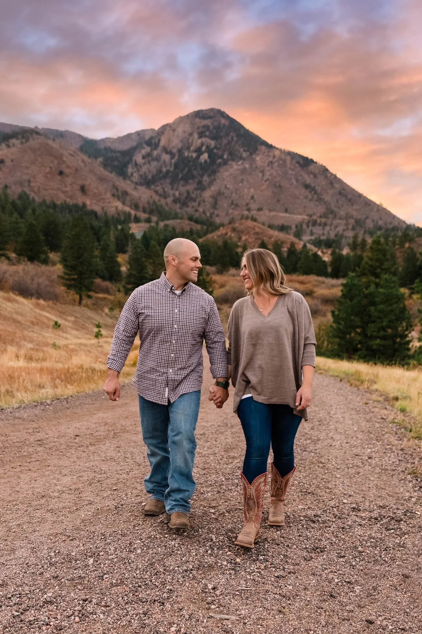 A couple walking hand in hand on a dirt trail in a mountainous area during sunset.