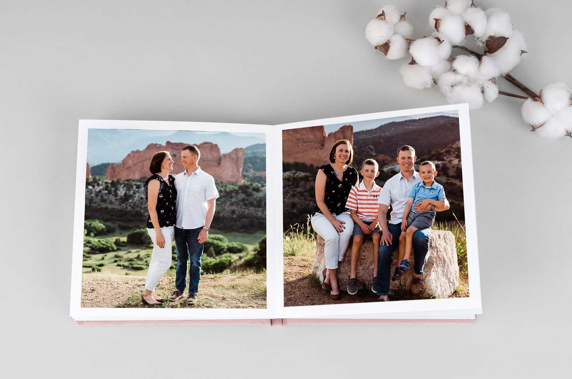 Open photo album with images of a couple walking and standing in a grassy field, holding hands in one photo and embracing in the other, with a branch of cotton flowers nearby.