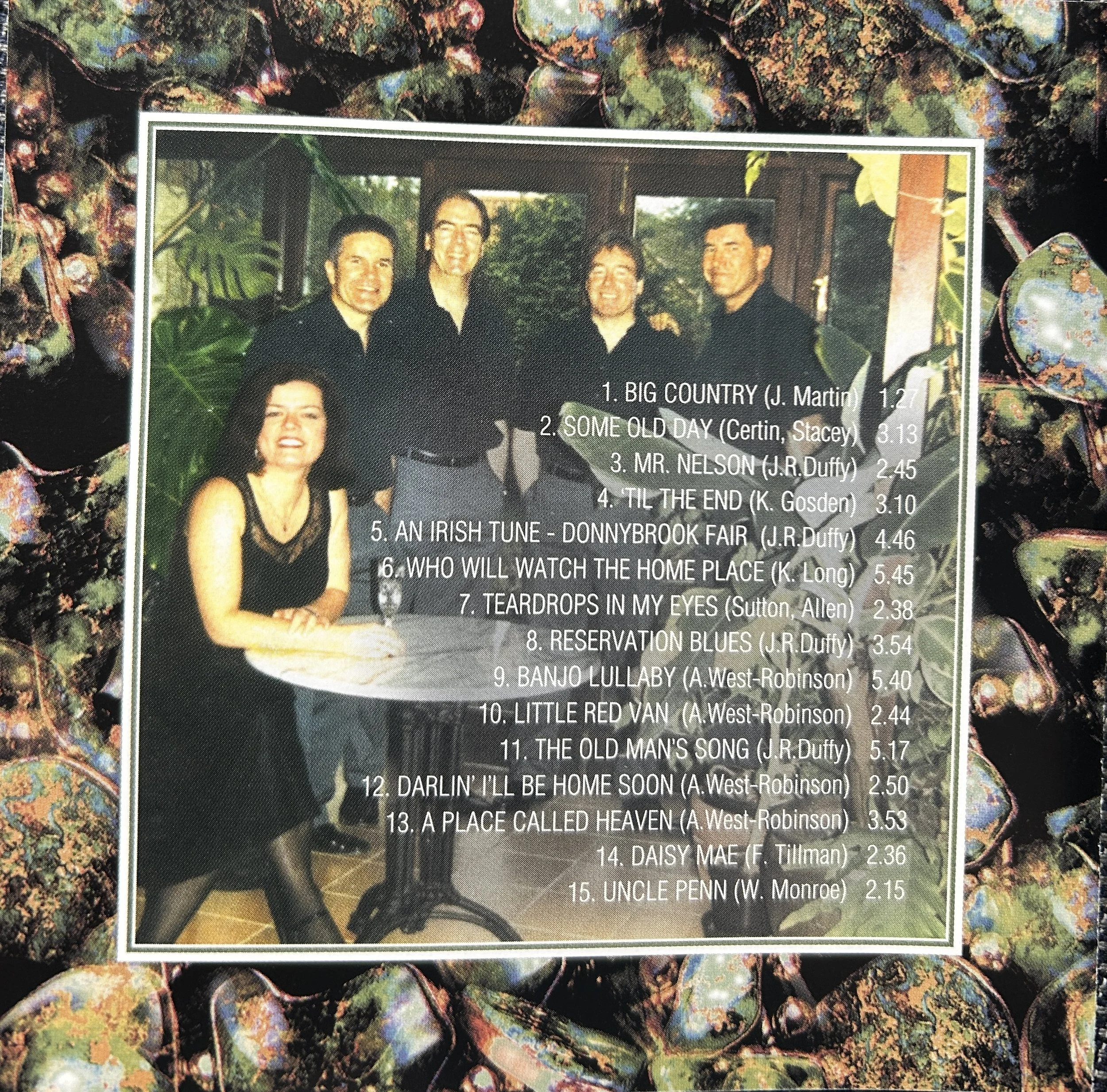 A group of five people, four men and one woman, smiling indoors behind a table with a leafy background. The image includes a tracklist overlay with song titles and durations.