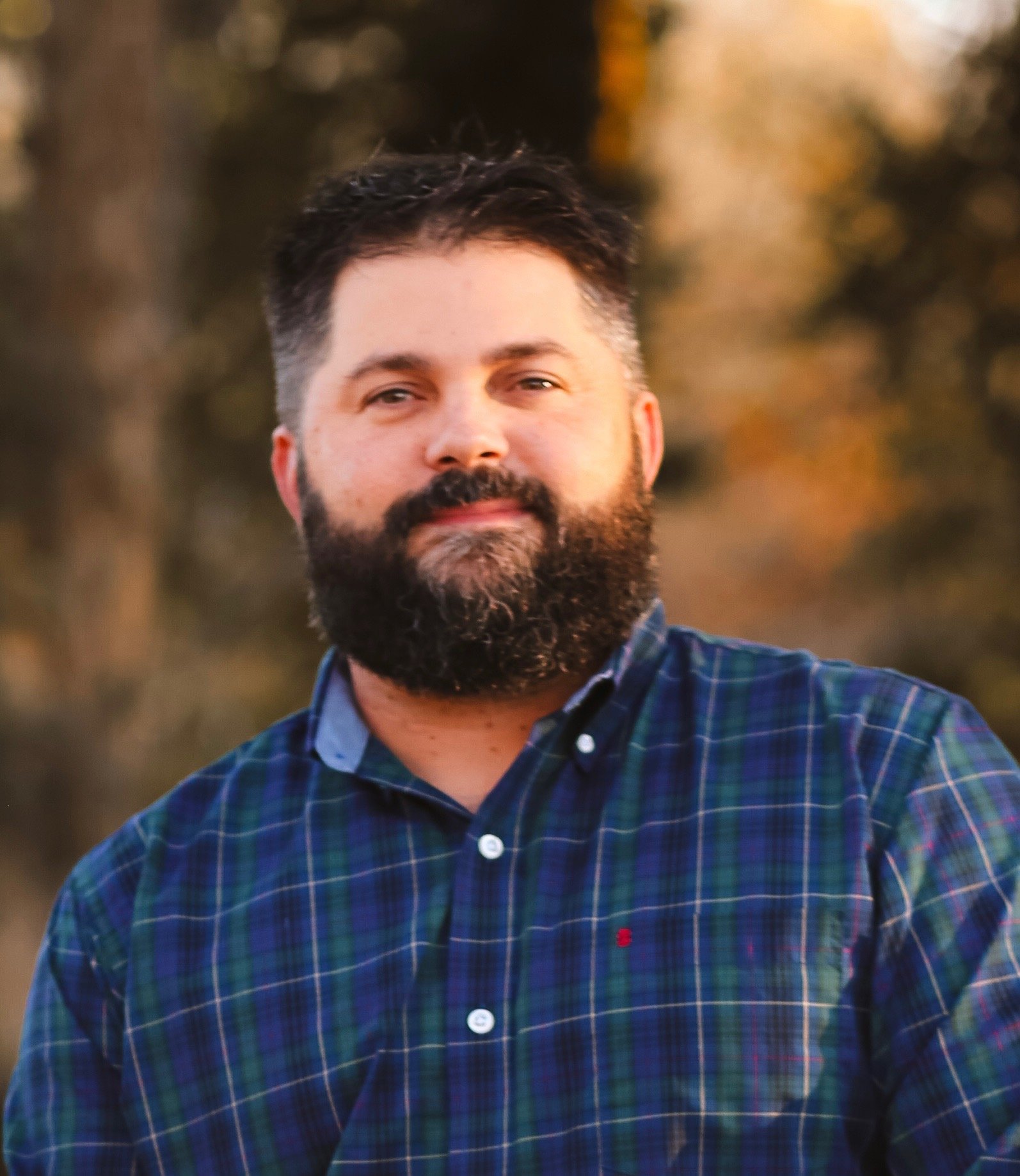 Man with glasses and beard wearing a dark sweater looking thoughtful indoors.