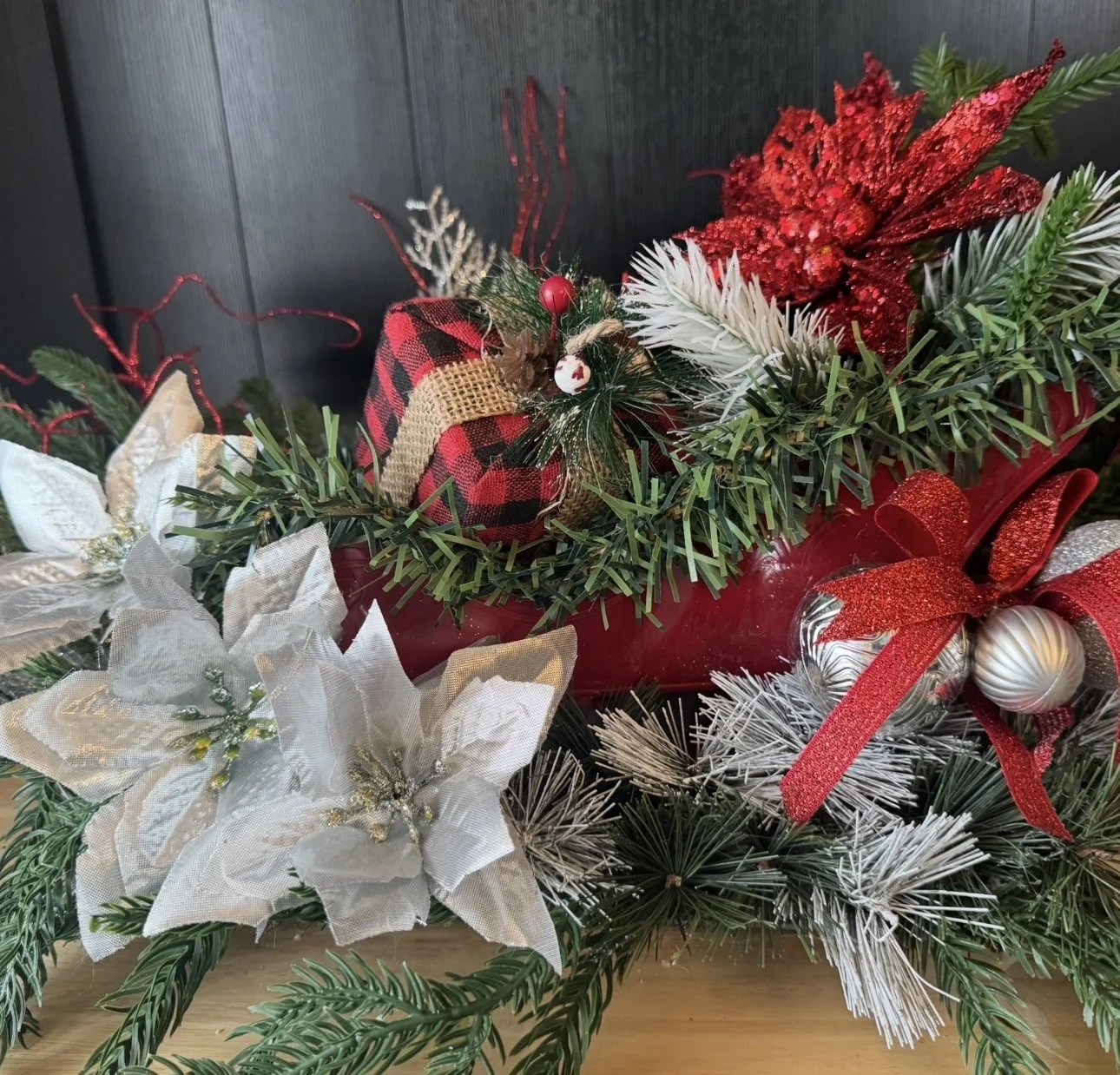 Christmas floral arrangement with poinsettia, white flowers, Christmas ornaments, greenery, and red ribbons.