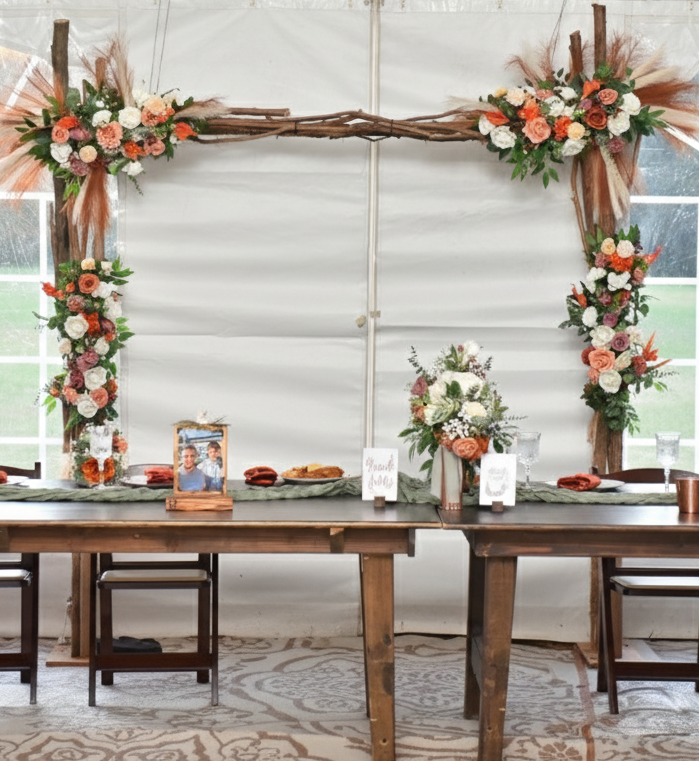 Wedding reception table with floral arrangements, a framed photo, and place settings under a rustic floral arch.