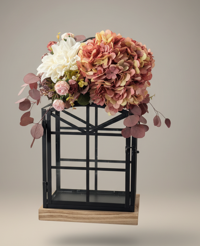 A floral arrangement featuring pink, white, and peach-colored flowers, including hydrangeas, placed on a black metal stand with a wooden base against a plain background.