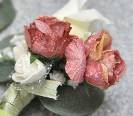 Artificial pink and white rose boutonniere with green leaves and a ribbon, on a gray surface.