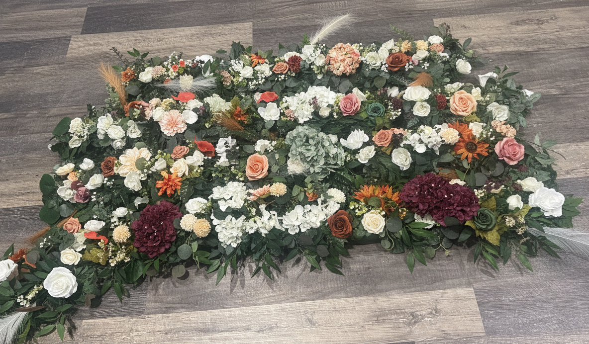 Arrangement of various flowers including roses, hydrangeas, and sunflowers, with greenery on a wooden floor.