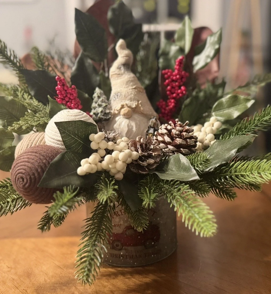 Christmas centerpiece with greenery, pinecones, a gnome figurine, and decorative berries in a container.