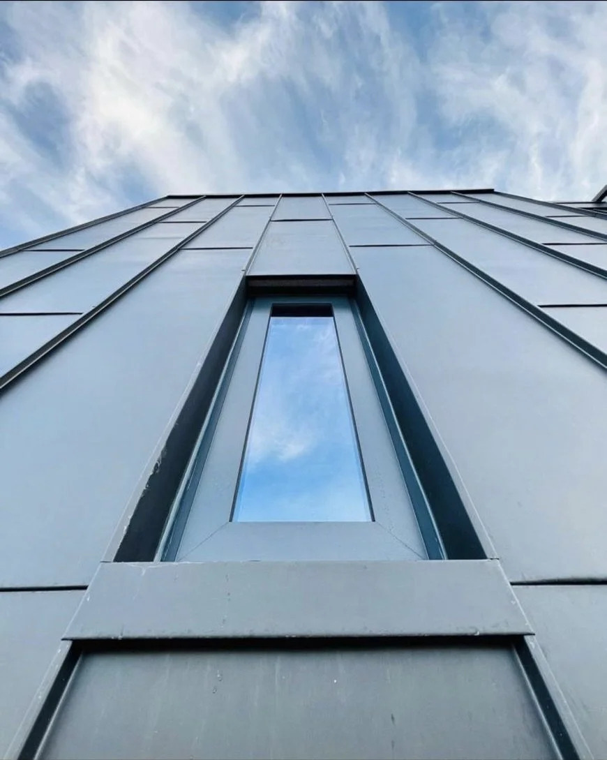 Tall modern building with narrow vertical window and cloudy sky.