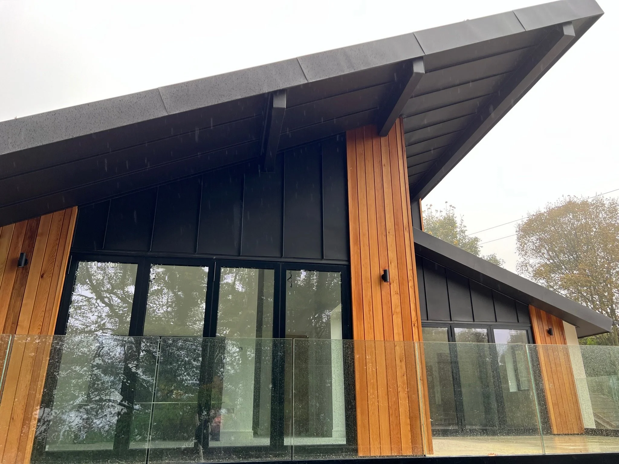 Modern house design with a sloped roof, wood paneling, large glass windows, and a glass balcony.