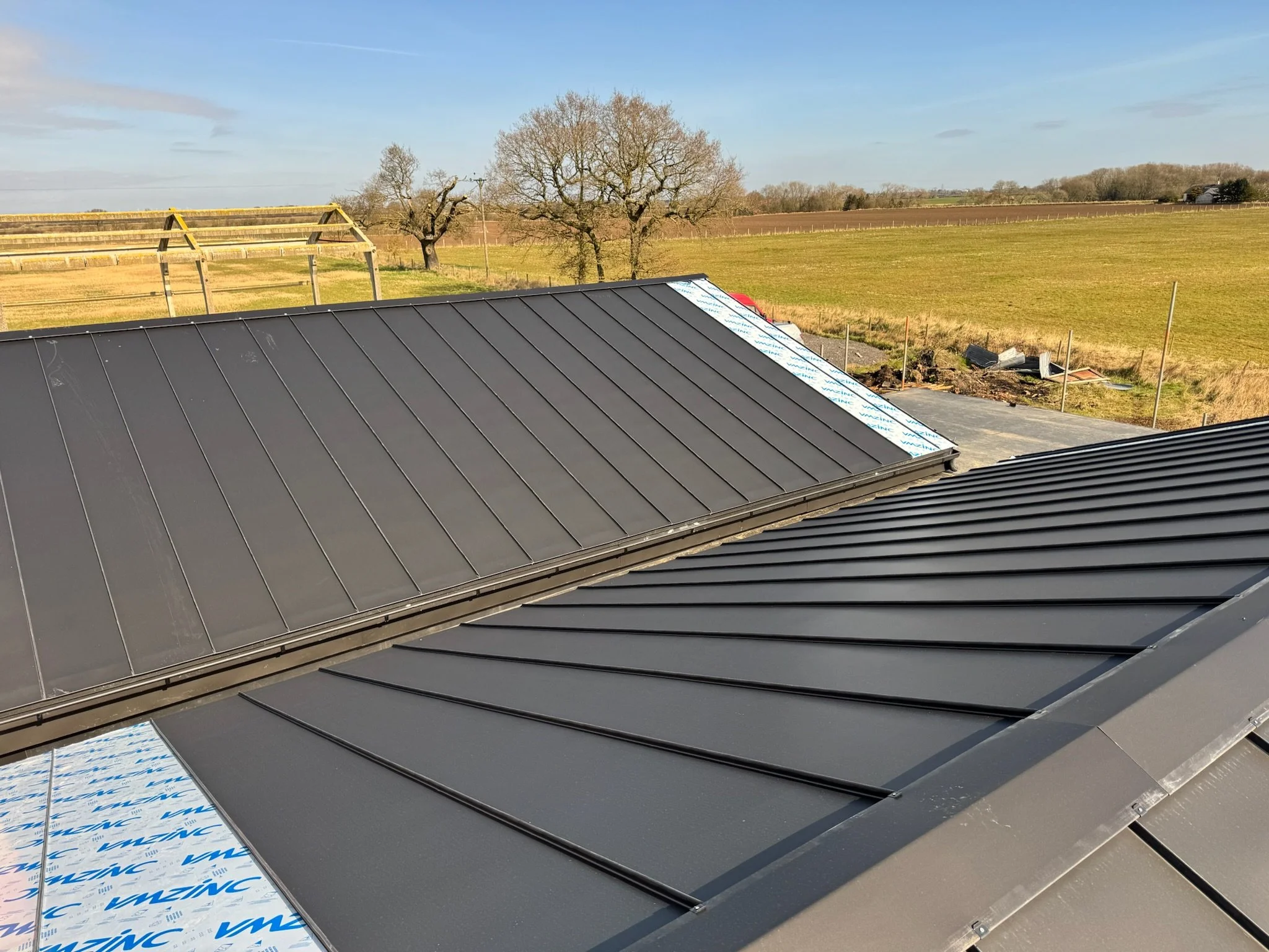 Metal roofing with greenery and trees in the background on a clear day.