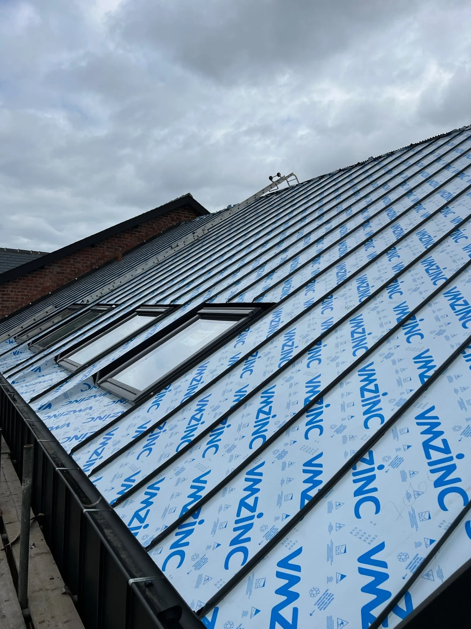 Metal roof covered with VMZINC panels and skylight windows under a cloudy sky.