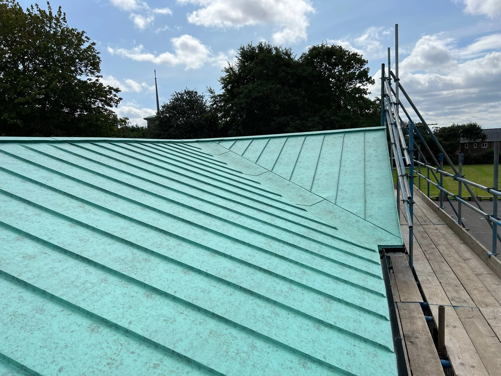 Green metal roof with standing seam design and scaffolding, under a partly cloudy sky