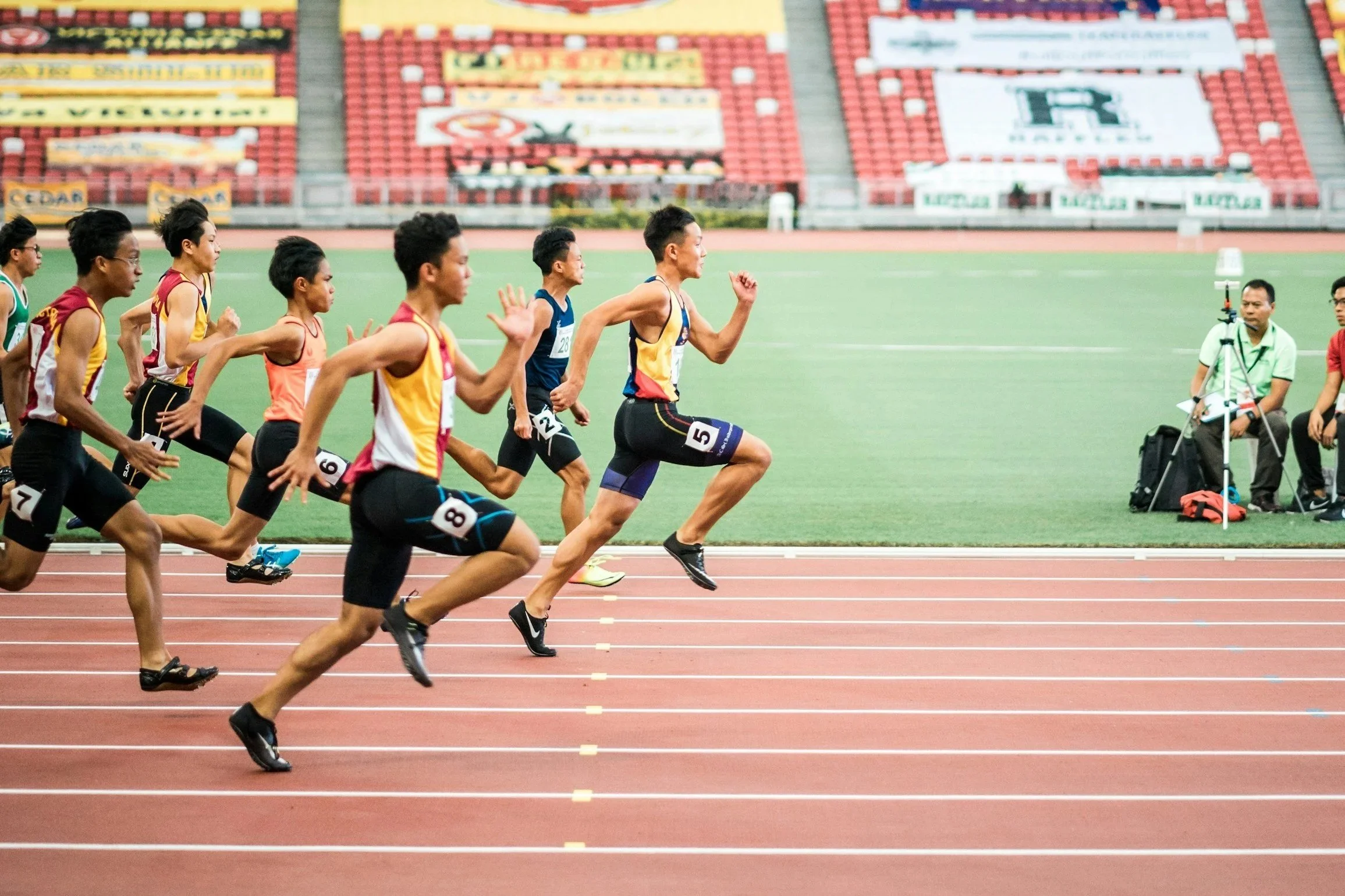 Track athletes running in a race on a red track at a stadium.