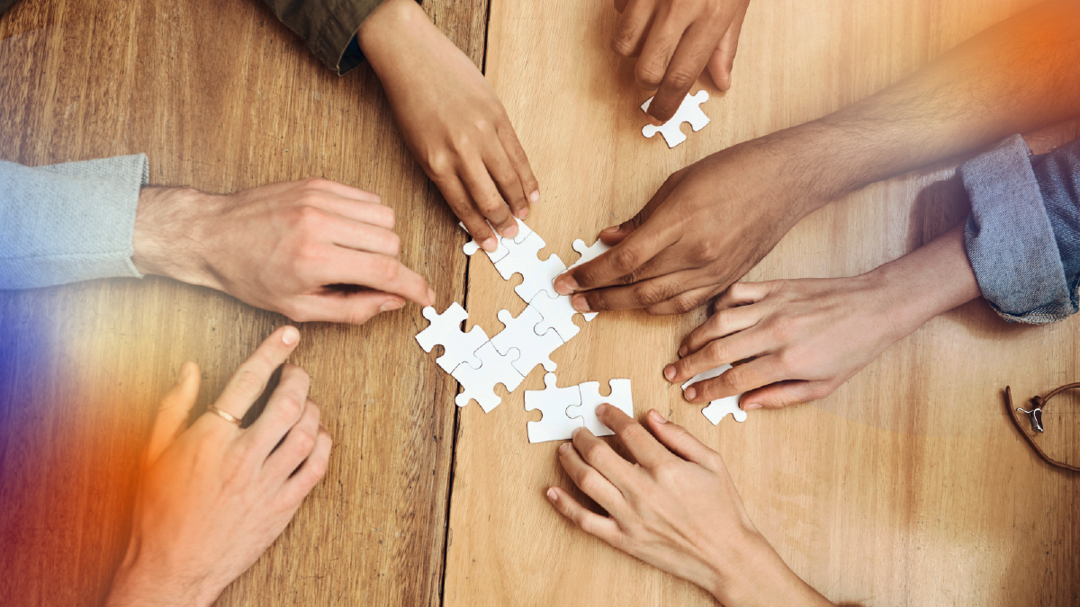 Mãos montando peças de quebra-cabeça sobre uma mesa, representando processos fragmentados e a falta de estrutura na gestão de clientes sem uma estratégia clara de CRM.