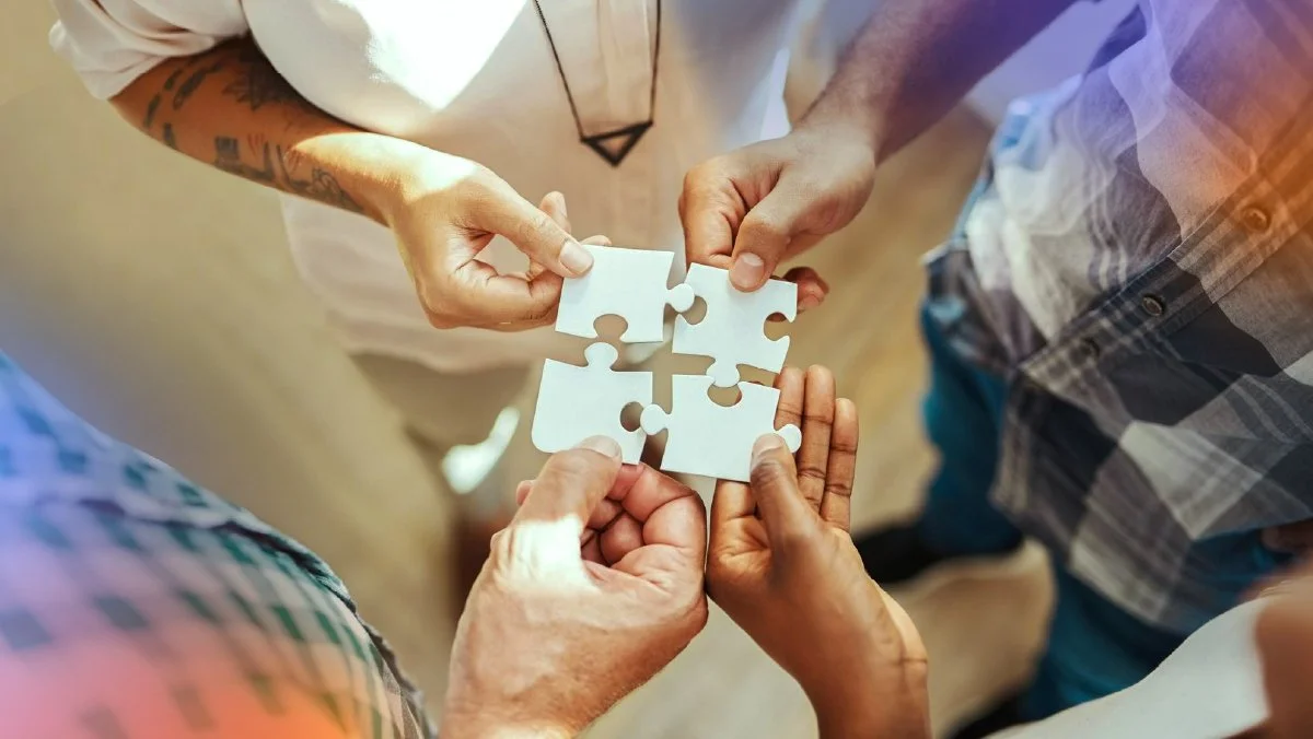 Diverse team members joining puzzle pieces together, representing the alignment of marketing, sales, and service through an integrated CRM system.
