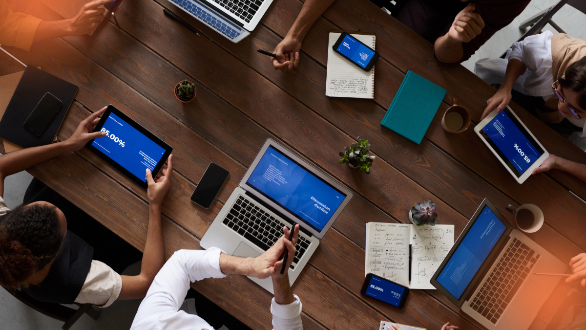 Team gathered around a conference table using laptops and tablets to analyze dashboards and business metrics, representing collaborative decision-making powered by Business Intelligence.