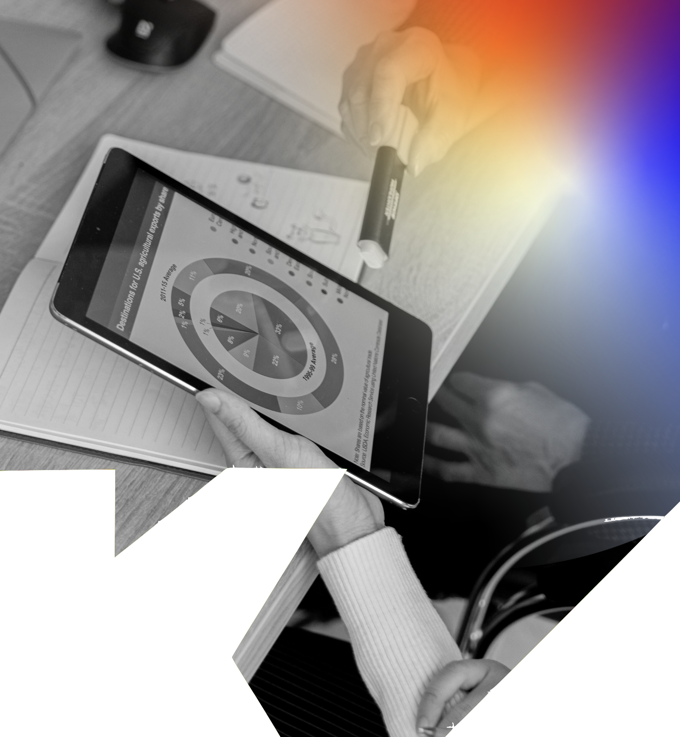 Person holding a tablet displaying a circular chart with statistical data, sitting at a desk with a notepad and a pen nearby, in an office setting.