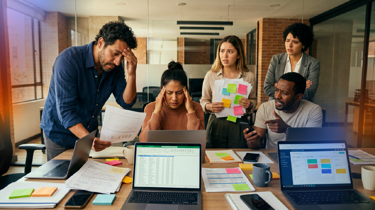 Stressed team surrounded by spreadsheets, sticky notes and multiple devices, representing disorganized customer management and operational overload without a centralized CRM system.