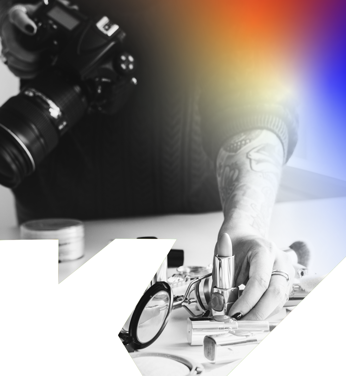 Person with tattooed arm arranging makeup items on a table, including lipstick, glasses, and powder, with a camera hanging from their neck.