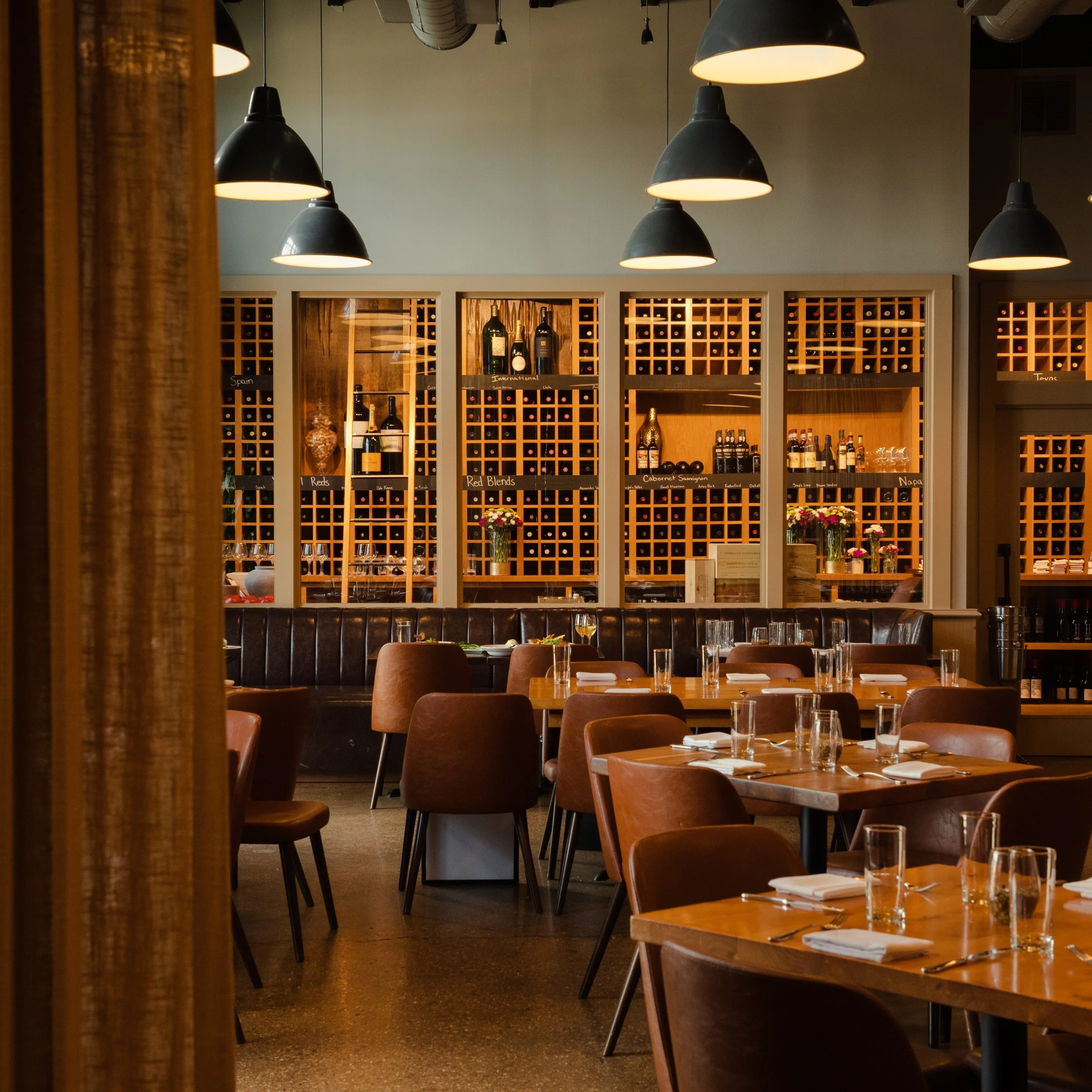 People dining in a rustic restaurant with brick walls, large windows, and modern lighting fixtures.
