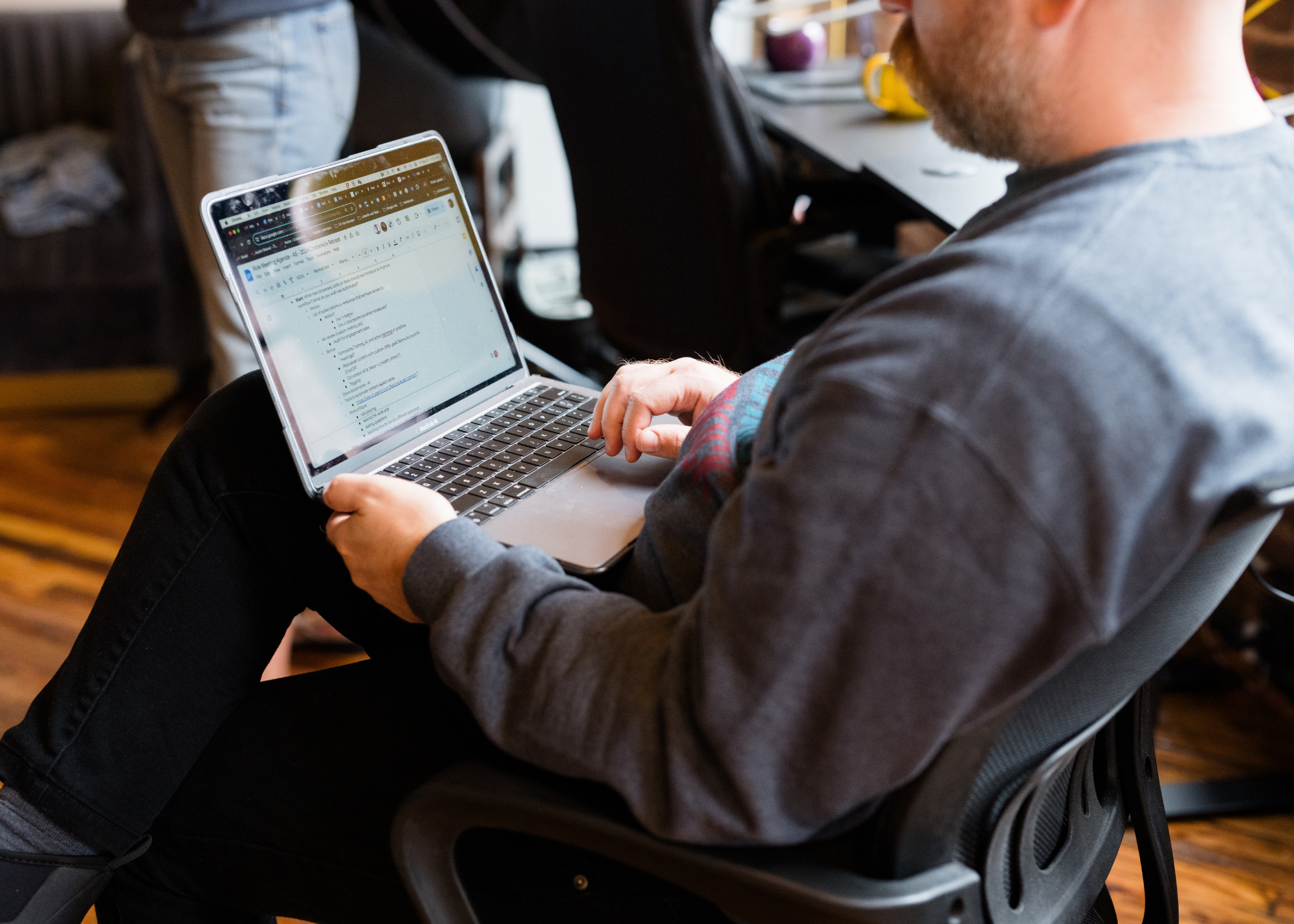 Person sitting in a chair using a laptop at a table in a room.