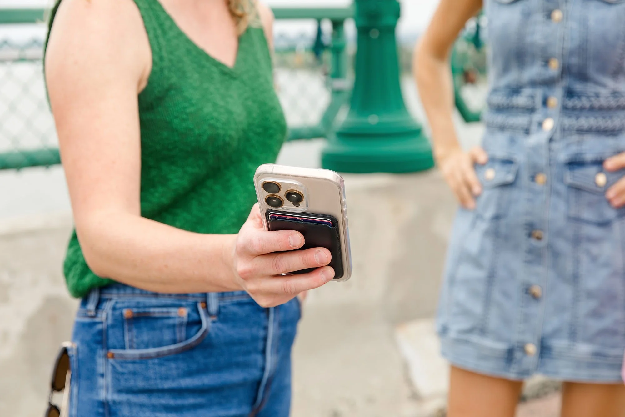 Two women standing outside near a green lamppost, with one woman holding a smartphone in her hand.