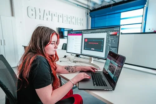 Young woman working on a laptop with dual monitors in a modern office setting.