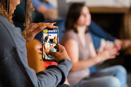 Person taking a photo of a woman with a smartphone in a cafe.
