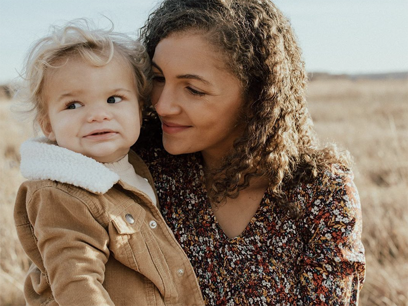 A woman and a young boy outdoors in a field, close together with the woman smiling and looking at the boy, who has a shy expression.