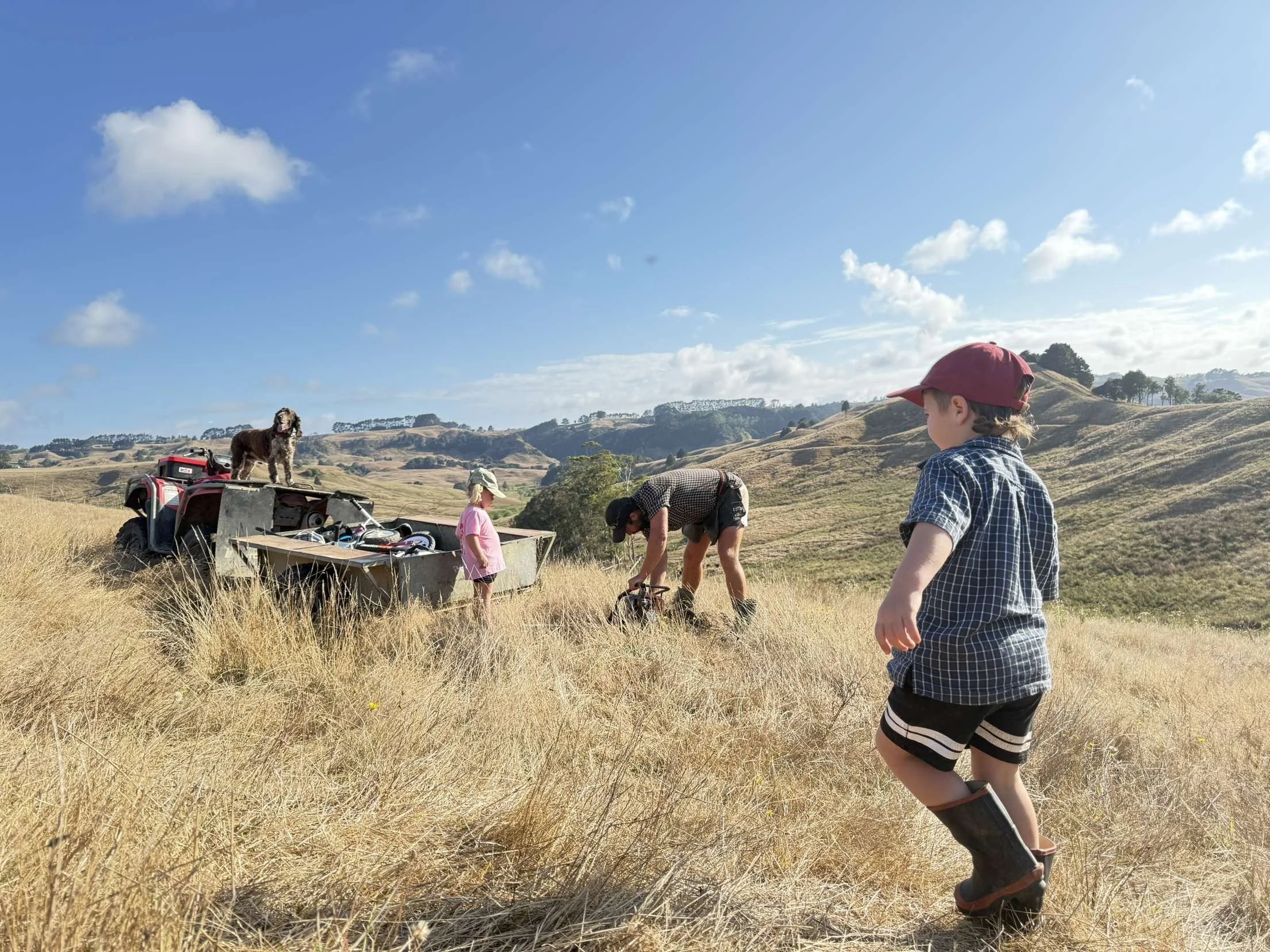 Local family and a dog on a hillside with a quad bike in the background while Boyd works on fencing maintenance on site.