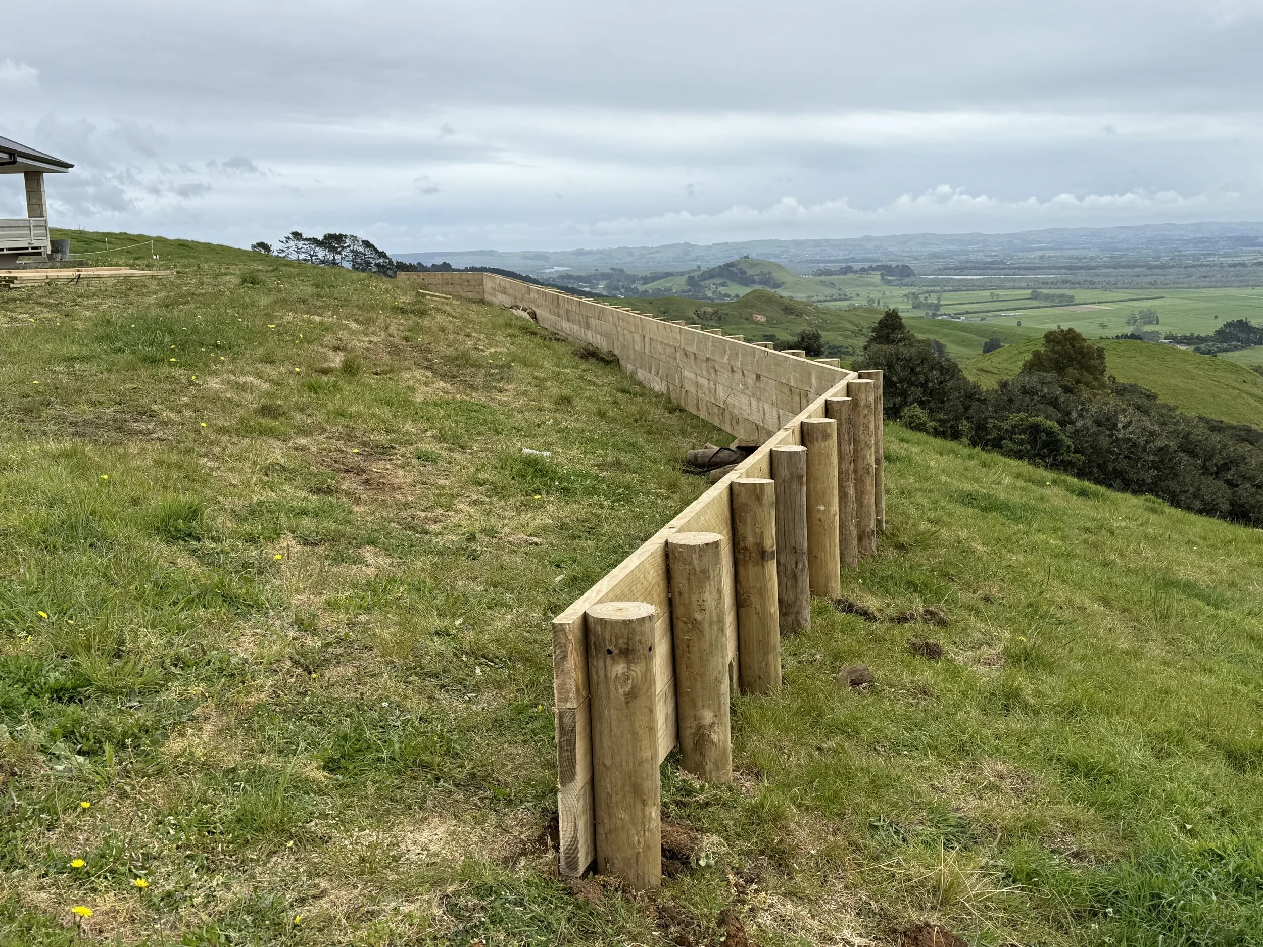 Landscape with a wooden retaining wall and grassy hills overlooking regional views