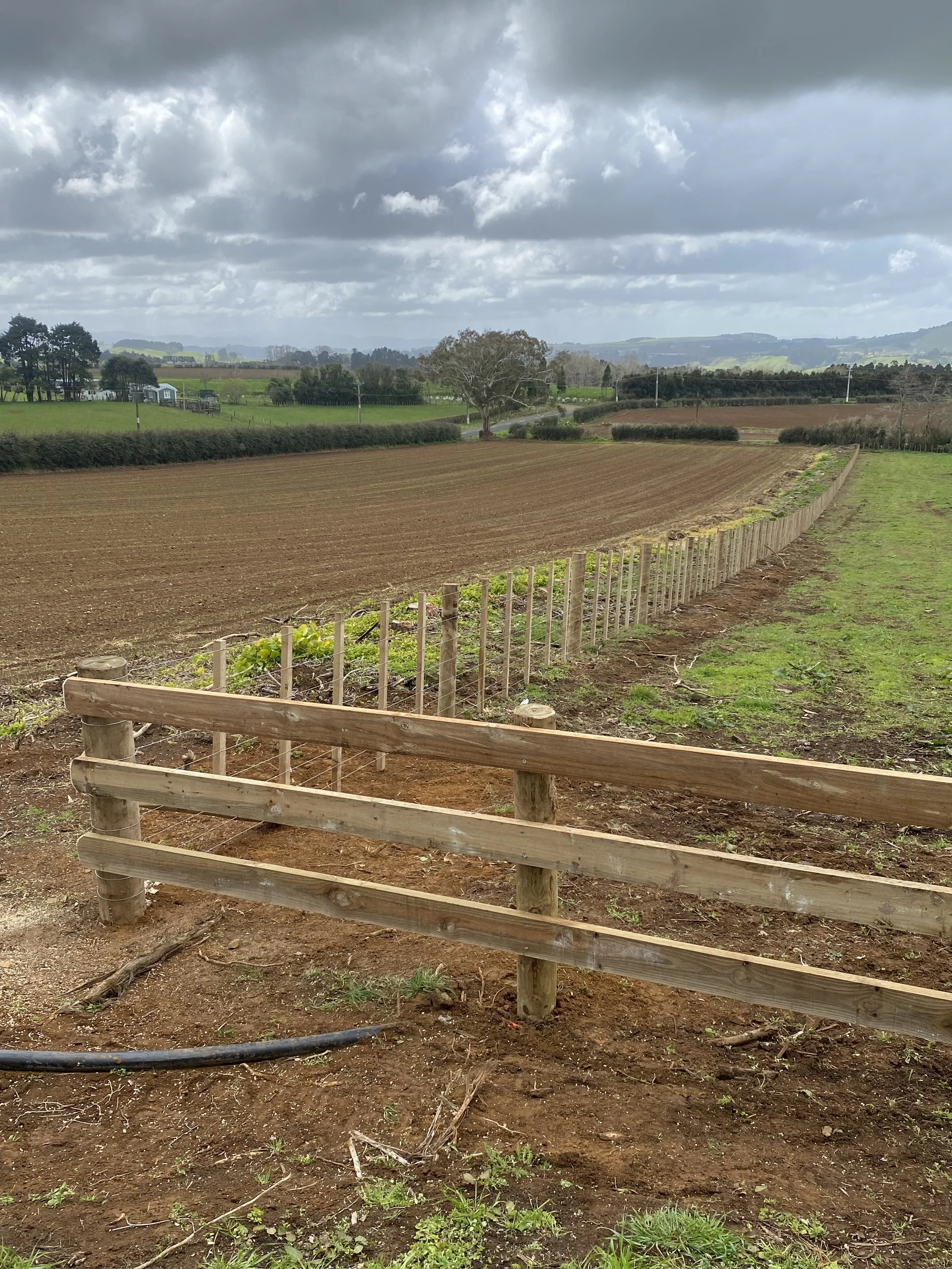 Plowed field with wooden fencing in a rural landscape, cloudy sky