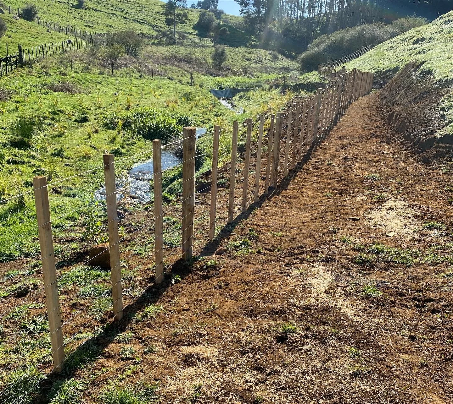 Wooden fence next to a dirt path and grassy field with trees in the background