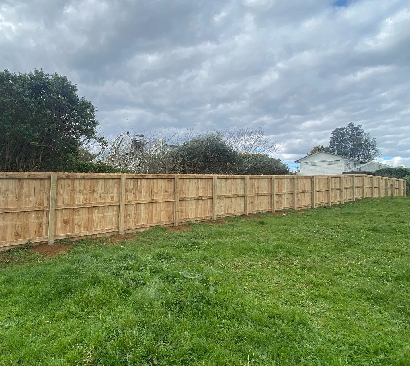 Wooden fence in a grassy yard with cloudy sky.