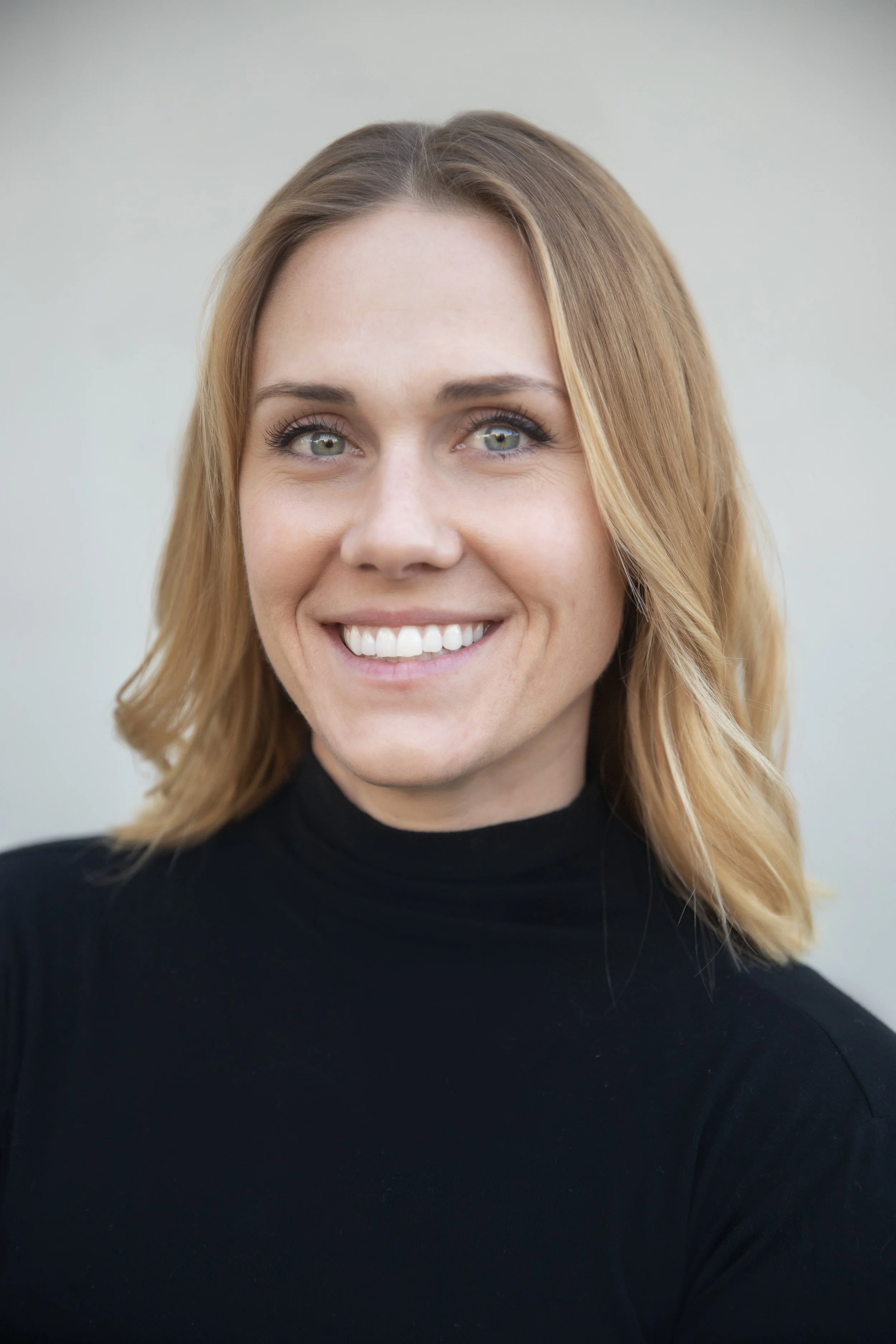 Close-up of Alison Shurter with shoulder-length wavy blond hair wearing a black turtleneck sweater.