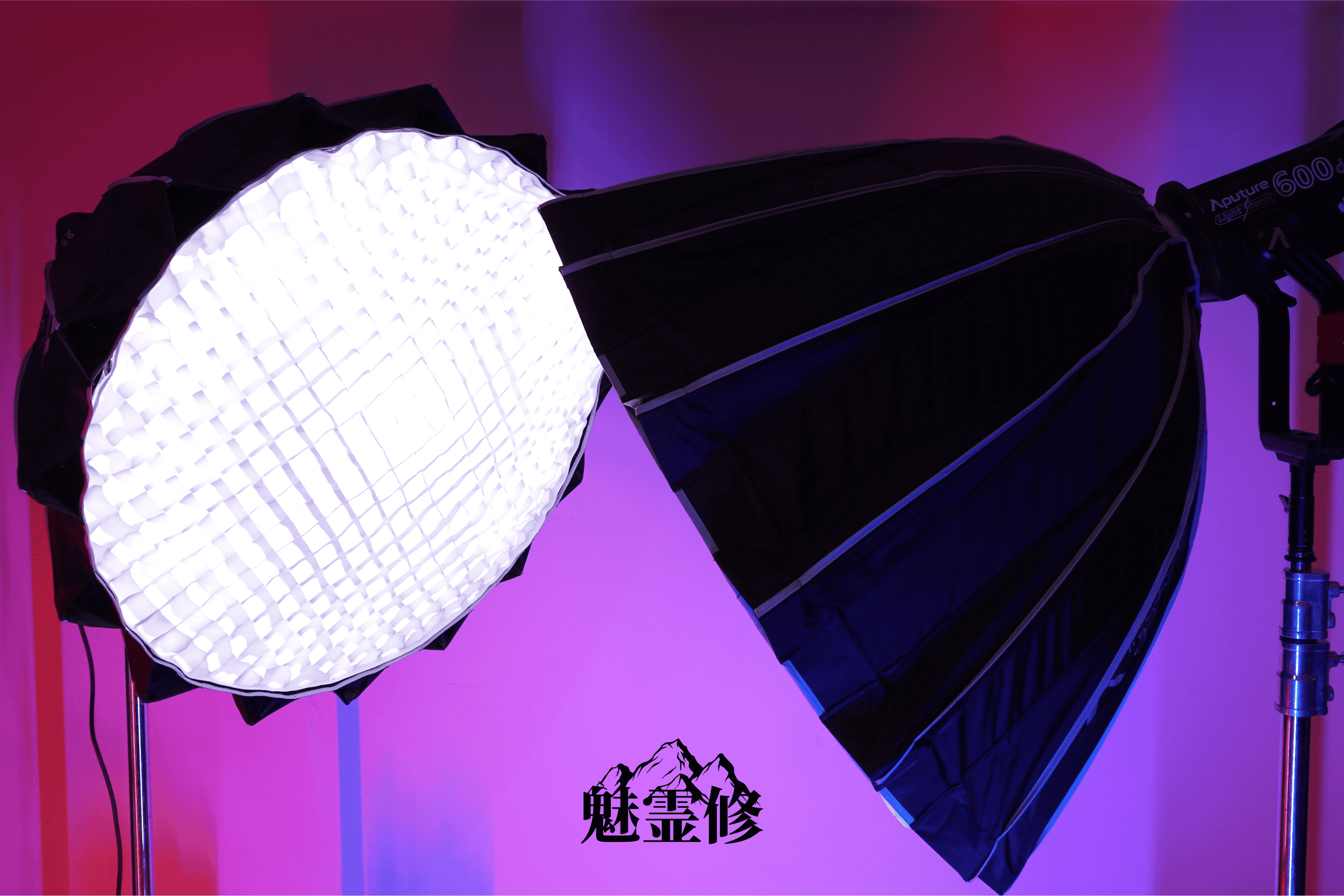 Studio lighting equipment including a softbox, a round LED light, and a backdrop with purple and pink gradient colors. There are Chinese characters and a mountain logo on the backdrop.