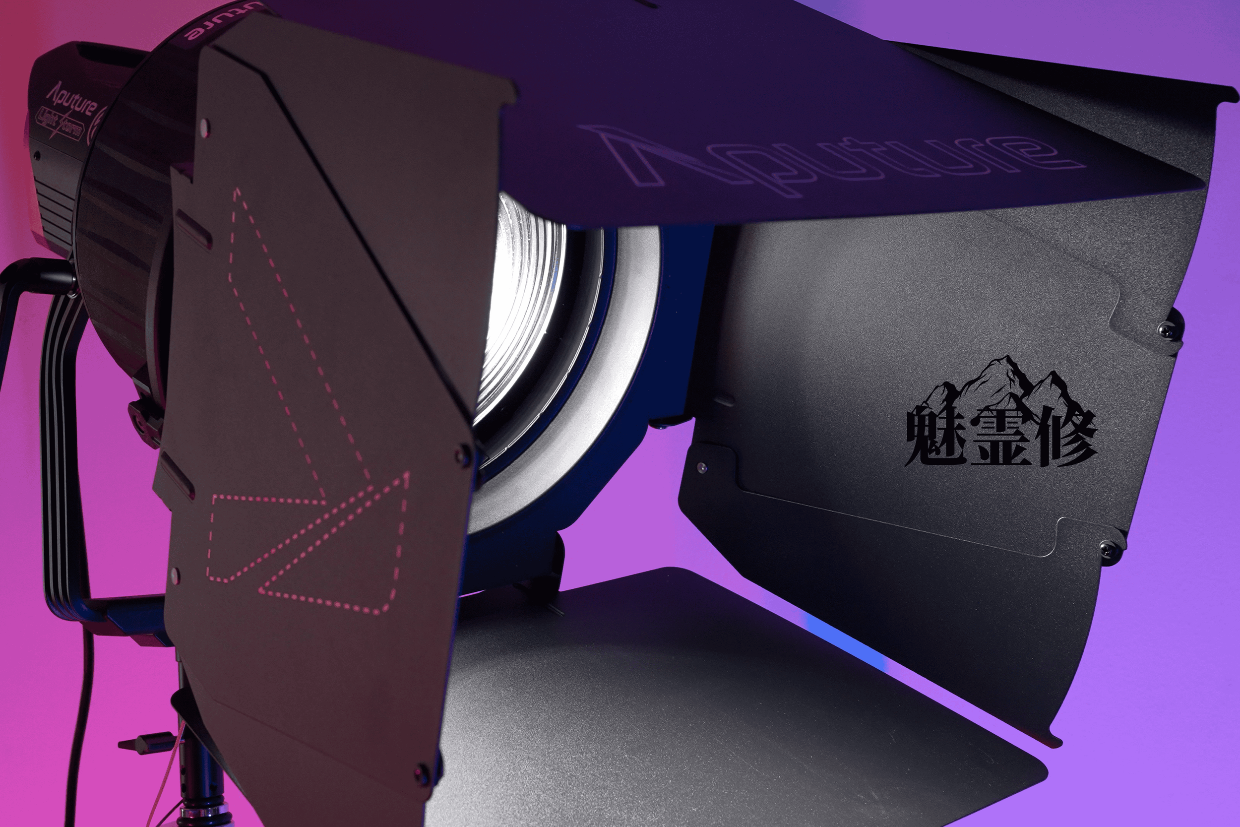 Close-up of a professional film or theater spotlight with adjustable hardware, black metal casing, and a lens emitting bright light, set against a vibrant purple and pink background.