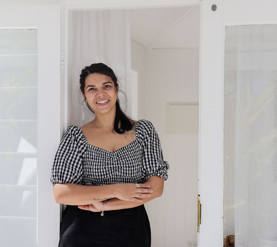 Person smiling at a doorway wearing a black and white checkered top with short sleeves.