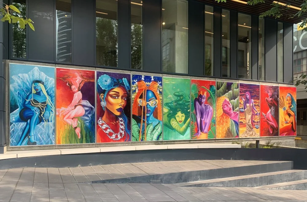 A series of colorful murals of various women painted on panels outside a modern building.