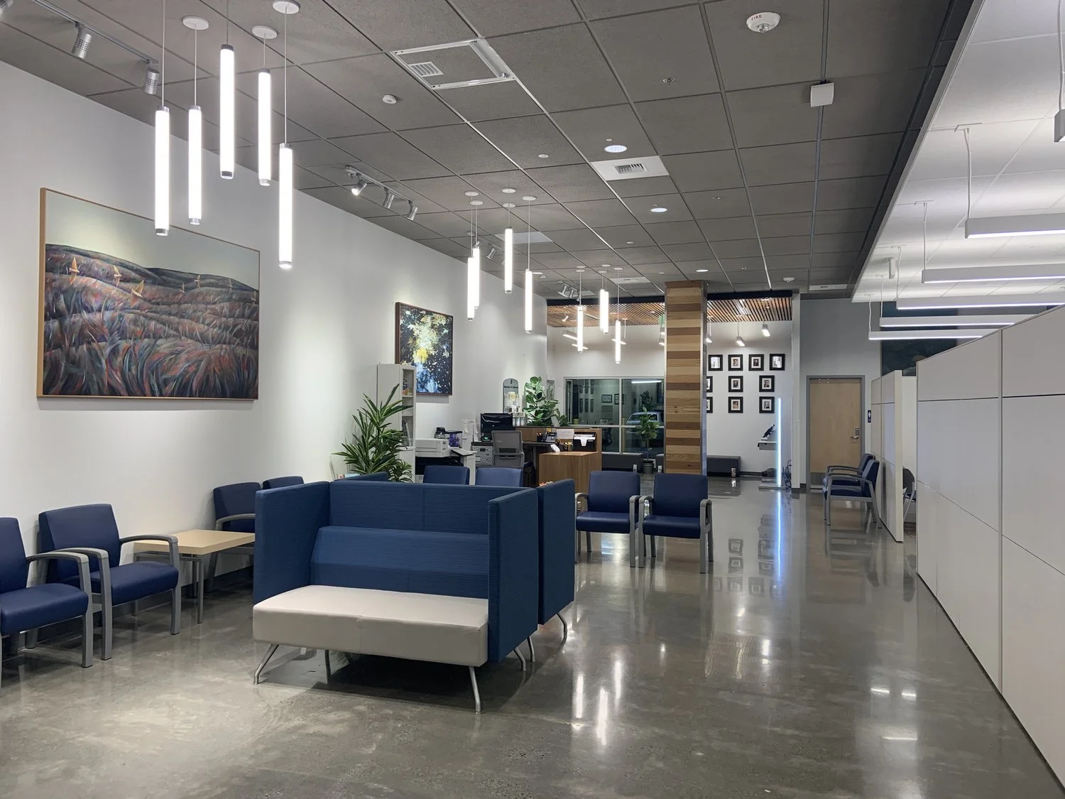 Modern office lobby with blue chairs, a seating area, art on the walls, and a reception desk in the background.