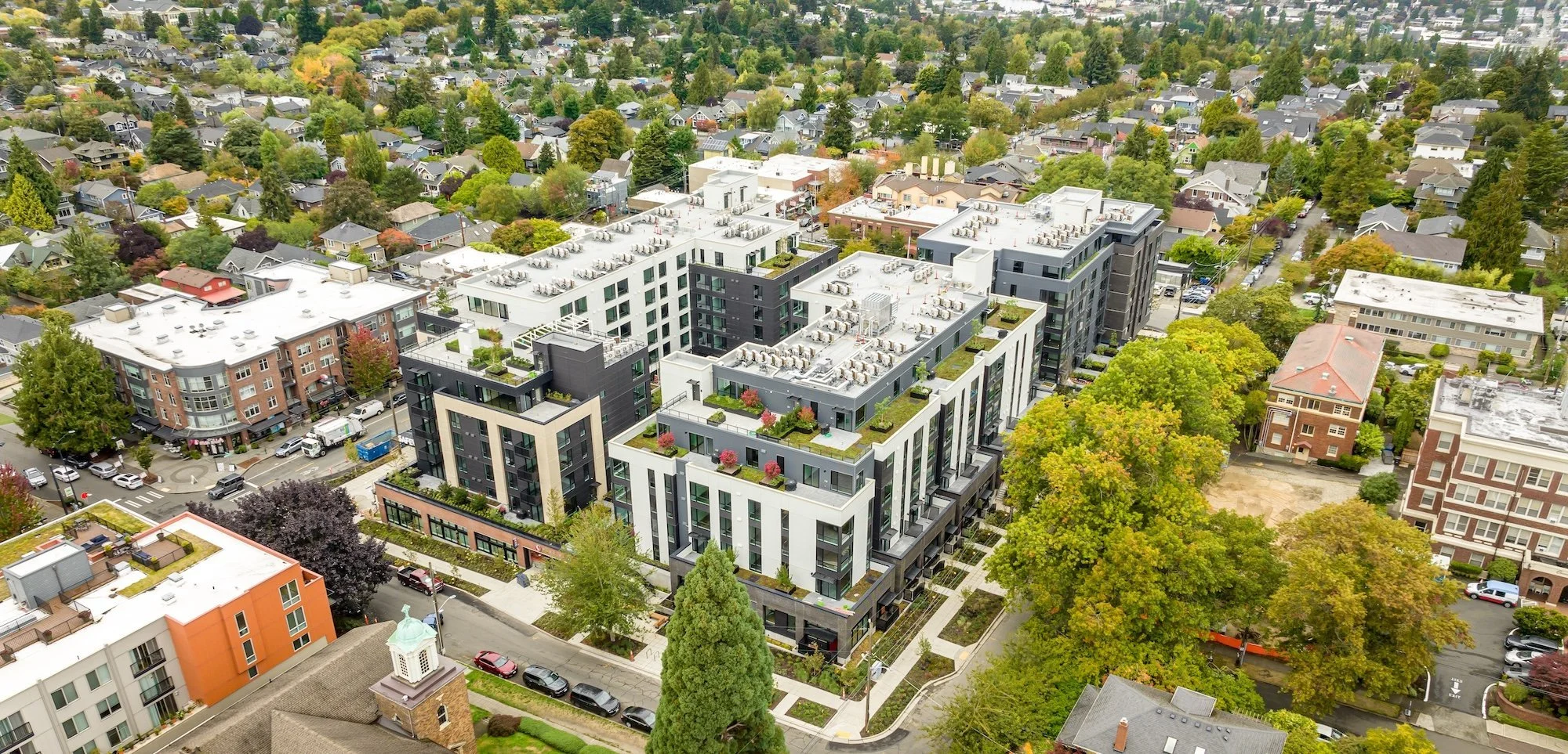 Aerial view of a modern apartment complex surrounded by trees and older residential neighborhoods.