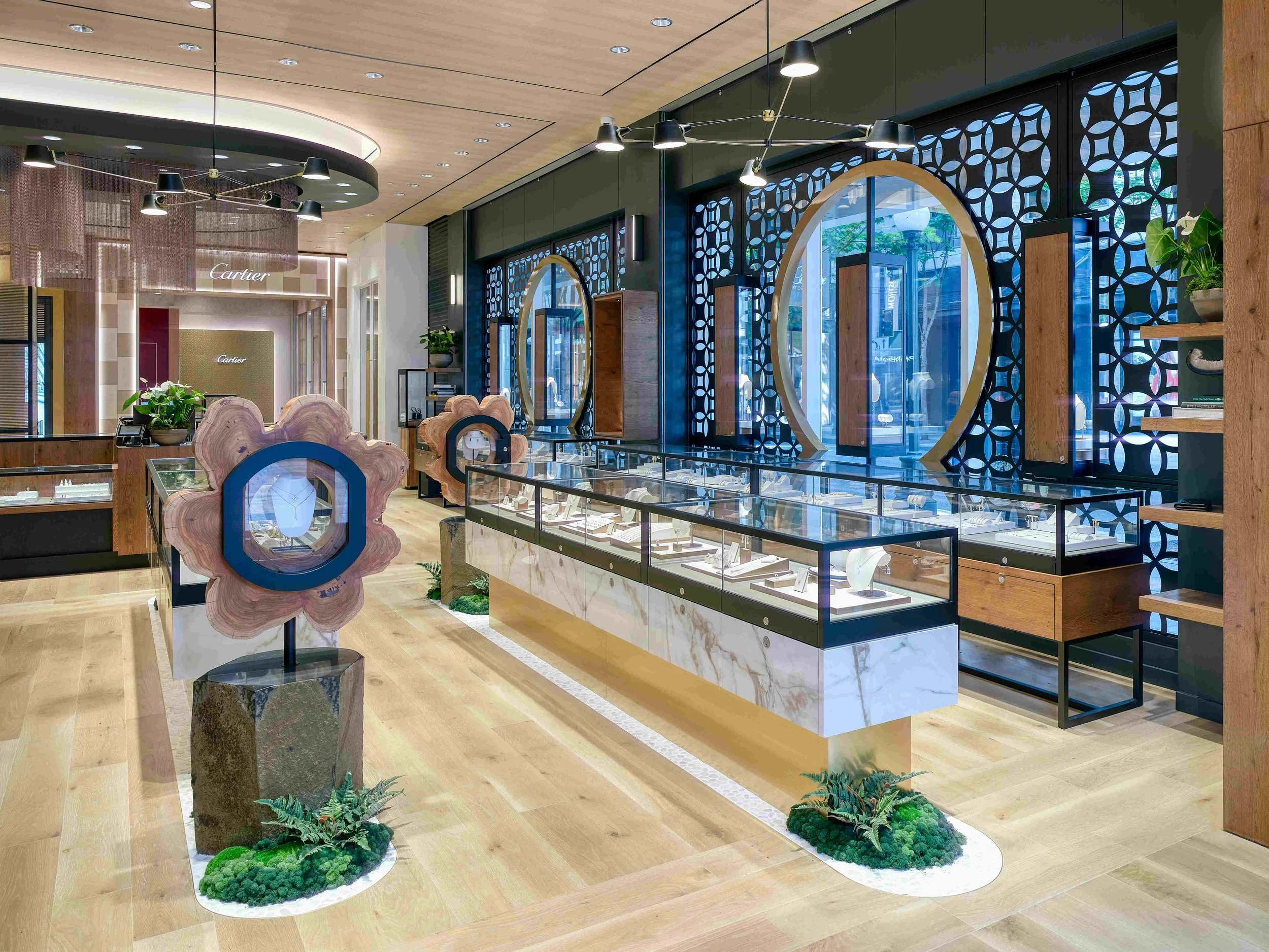 Interior view of a jewelry store with display cases, wooden and marble accents, decorative mirrors, and plants.