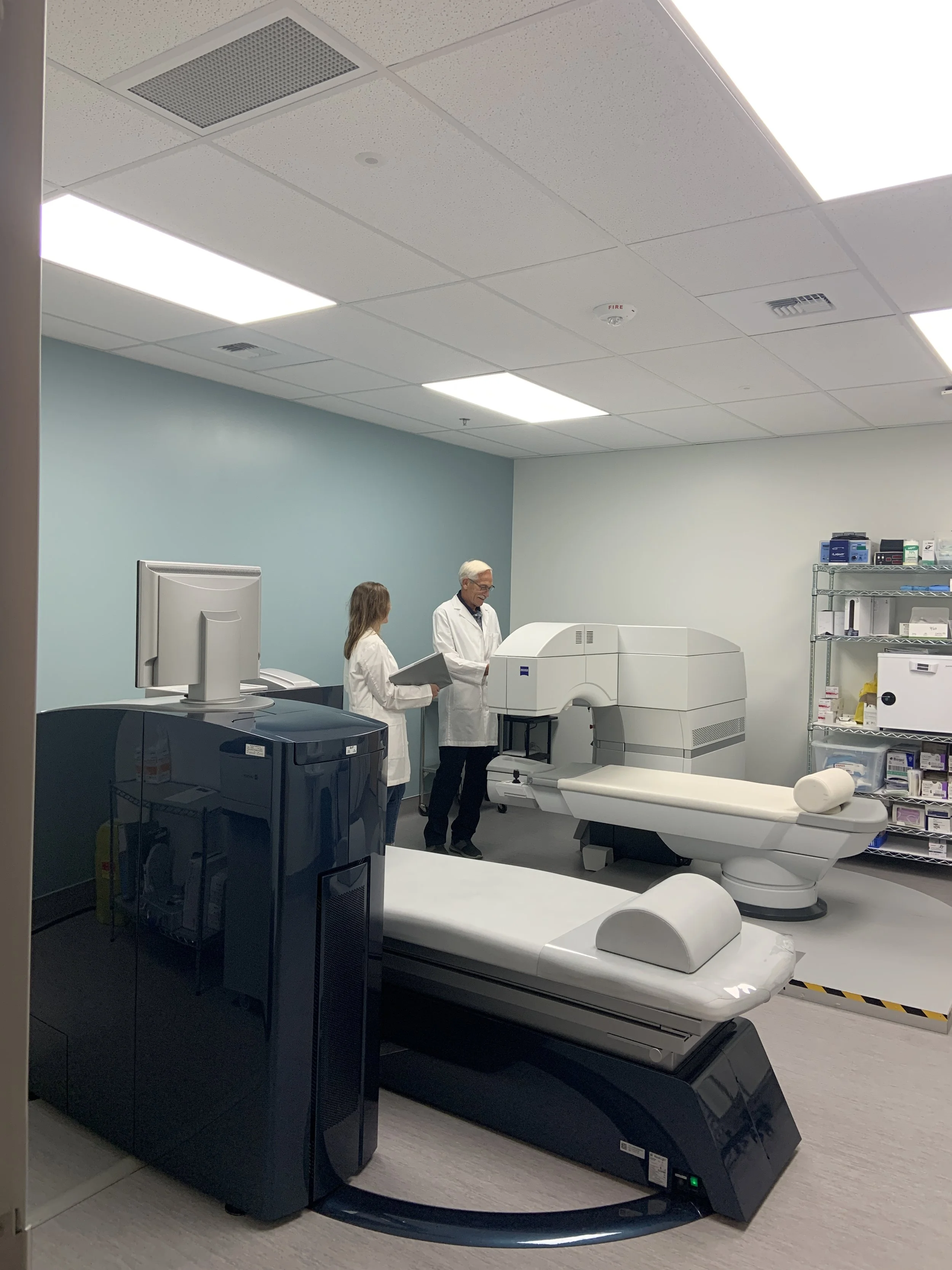 Medical imaging room with a large MRI machine, staff in white coats, and medical supplies on shelves.