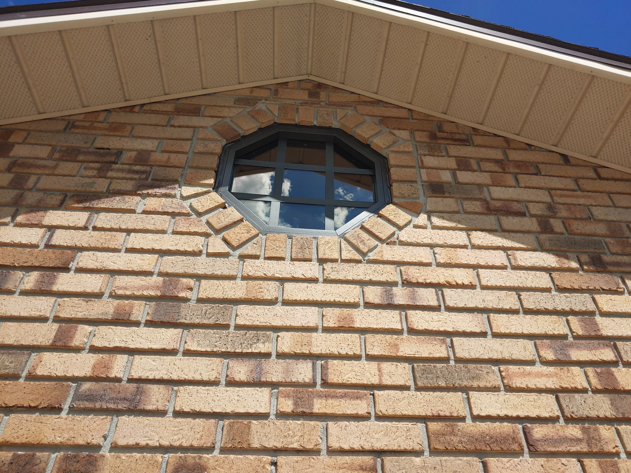 Brick exterior wall with an octagonal window installation replacement. Perfect bronze caulking