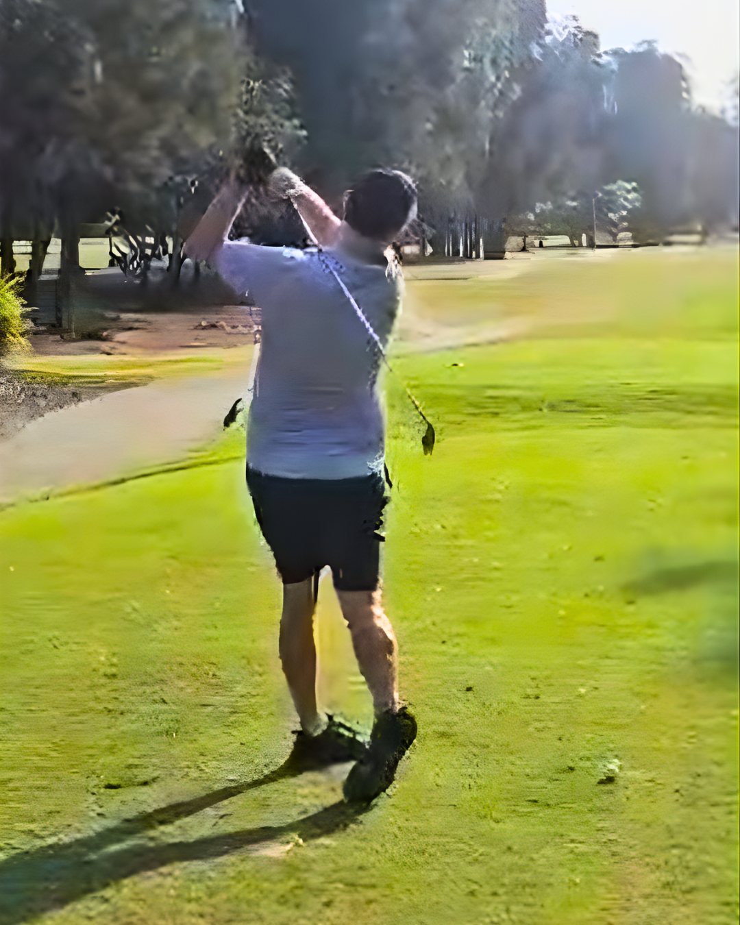 A person on a golf course swinging a golf club, with trees and grass in the background.