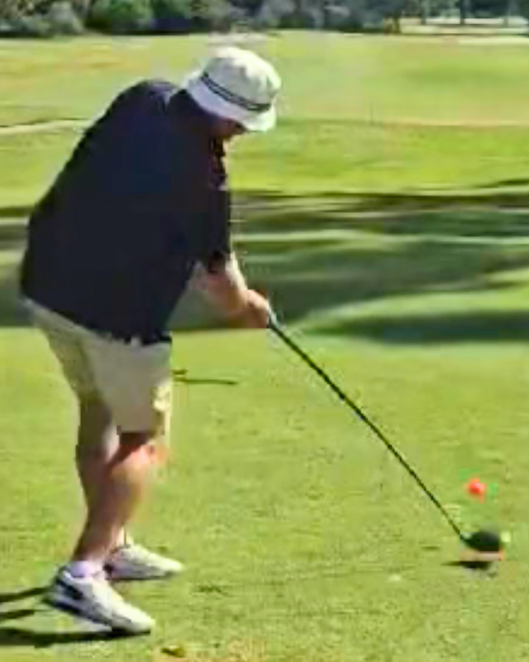 A person preparing to hit a golf ball on a golf course, wearing a white hat, black shirt, and shorts.