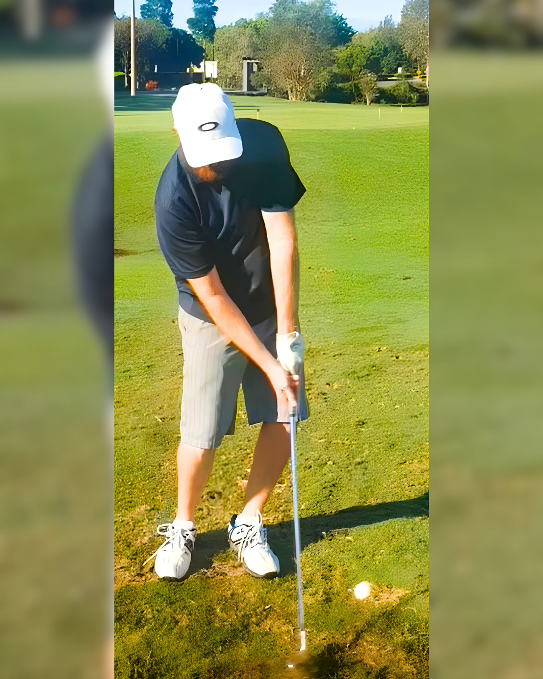 A man playing golf on a golf course, preparing to hit a golf ball from a sand trap or bunker, wearing a white cap, black shirt, striped shorts, and white shoes.
