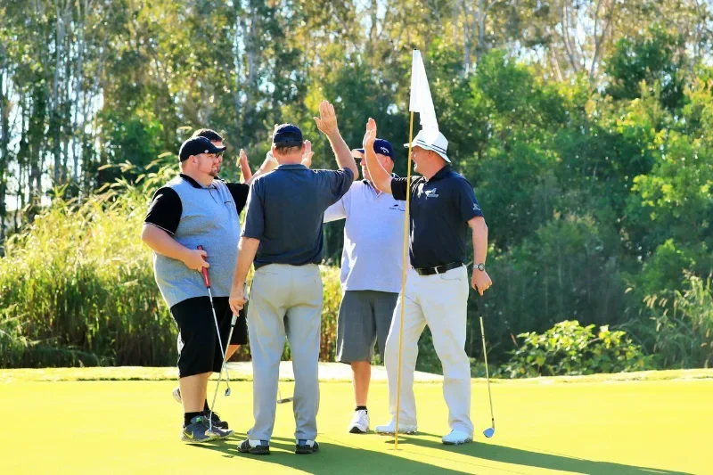 Group of five men at Emerald Lakes golf course celebrating a putt, with Paul Williamson Golf Coach in one of his Play with The Pro Experiences instead of a golf lesson