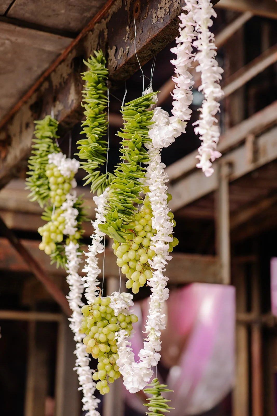 Hanging flower garlands with green leaves, white flowers, and green berries, displayed on wooden beams in a rustic setting.