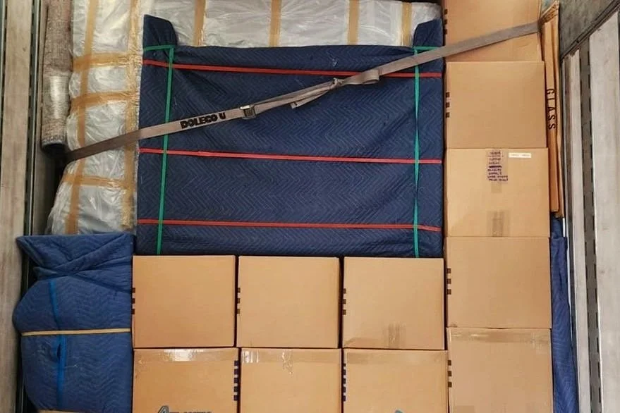 Boxes and furniture wrapped in moving blankets, secured inside a truck with straps.